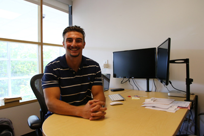 Student smiles in front of computer in office setting